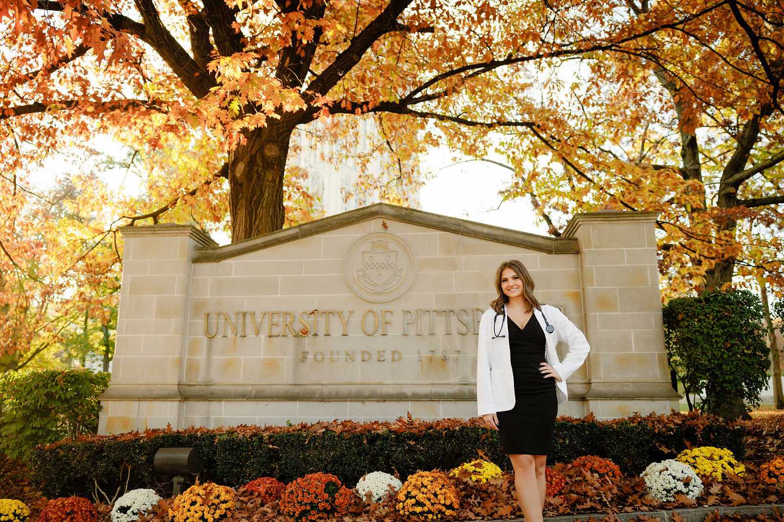 College Graduate standing in front of the sign for the University of Pittsburgh