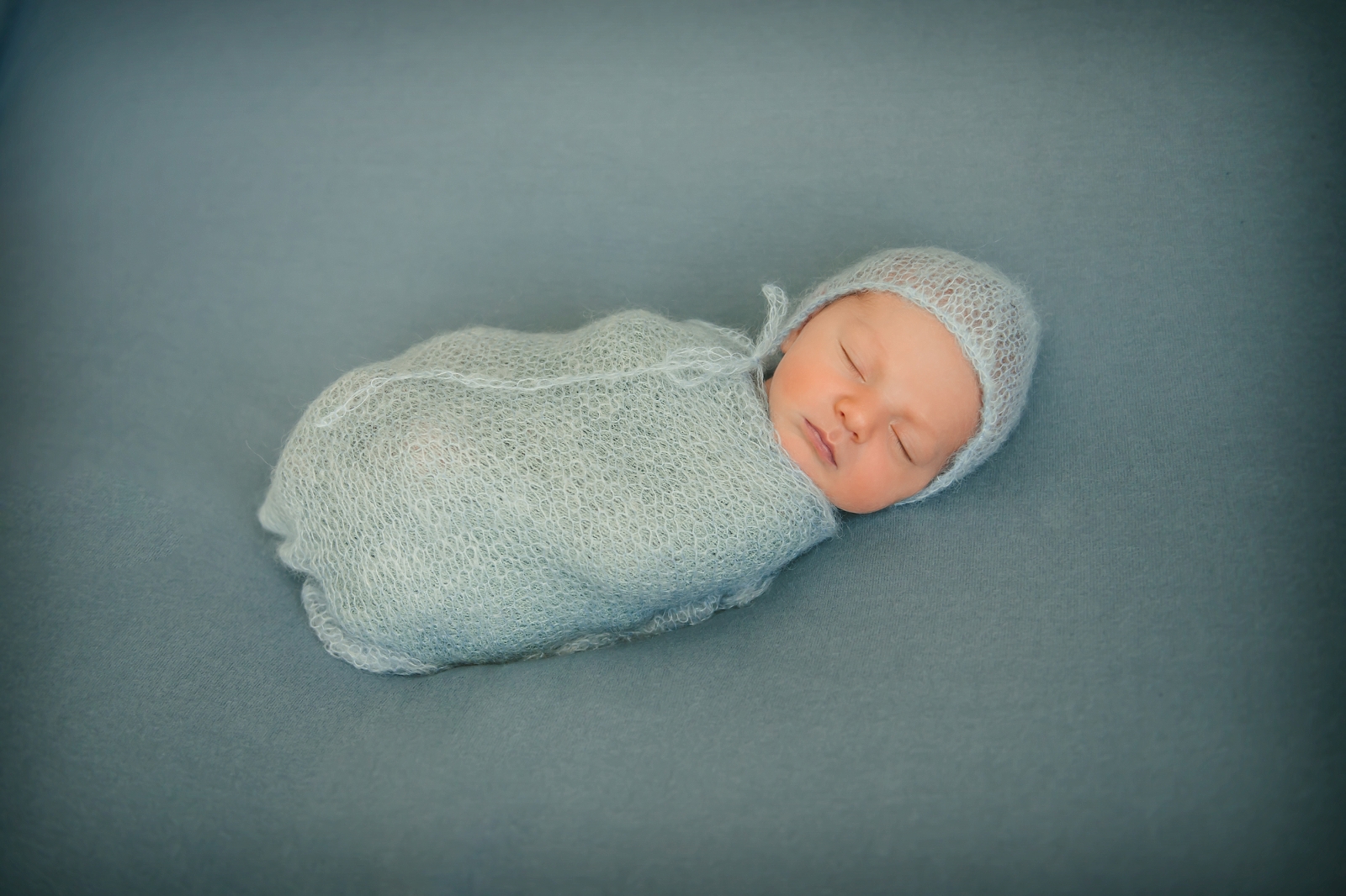 Newborn baby boy wrapped in blue wrap laying on blue blanket in photography studio in Moon Township near PIttsburgh