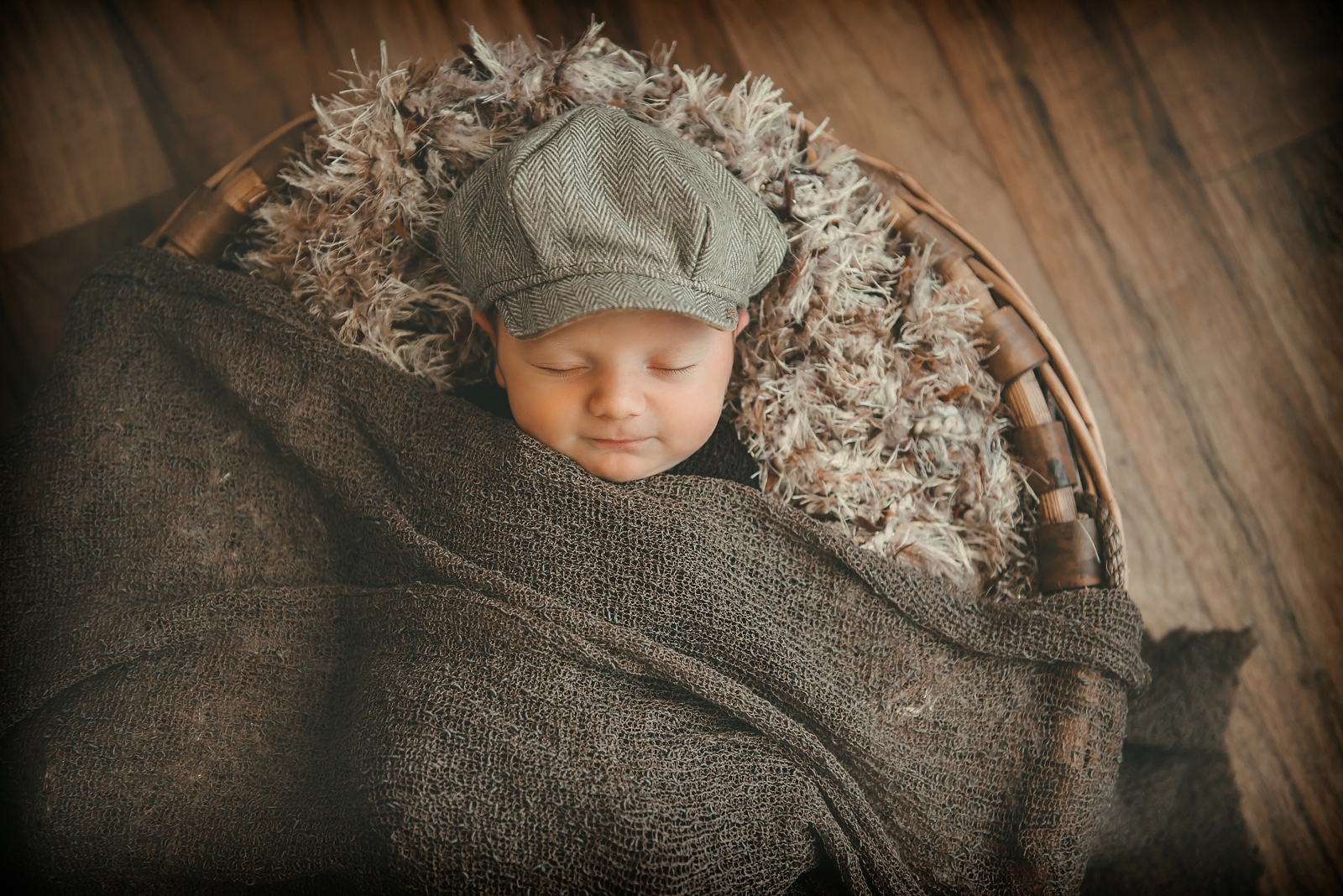 Newborn baby boy wearing brown hat in brown basket in photography studio in Moon Township near Pittsburgh