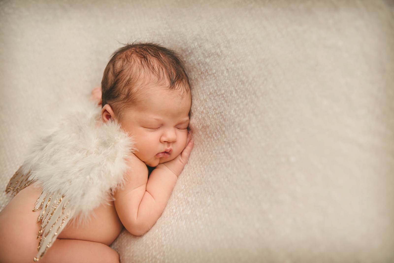 Newborn baby girl laying on cream blanket and wearing wings in photography studio in Moon Township near Pittsburgh