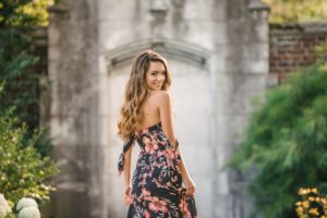 High school senior girl looking over shoulder in front of stone wall in Mellon Park near Pittsburgh