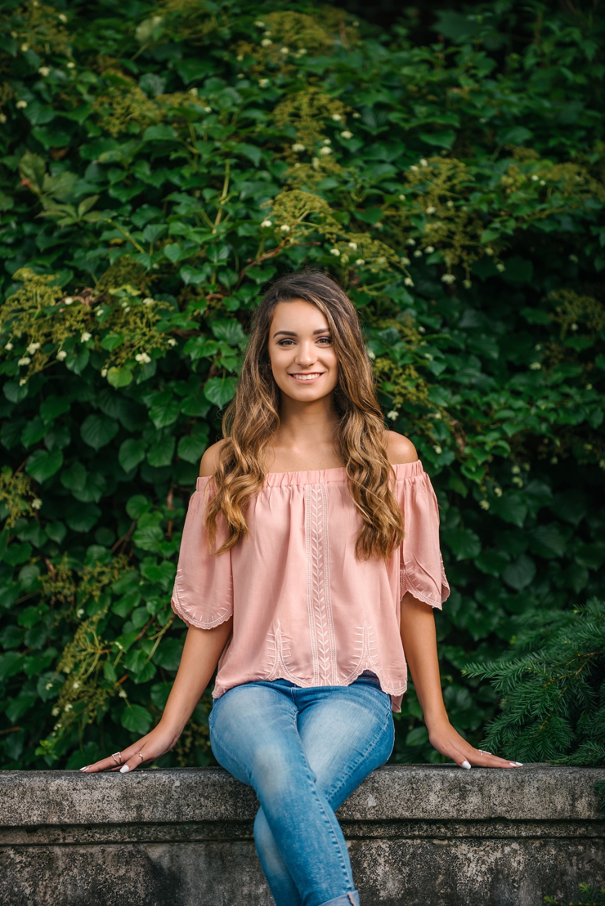 High school senior girl sitting on stone wall at Mellon Park near Pittsburgh