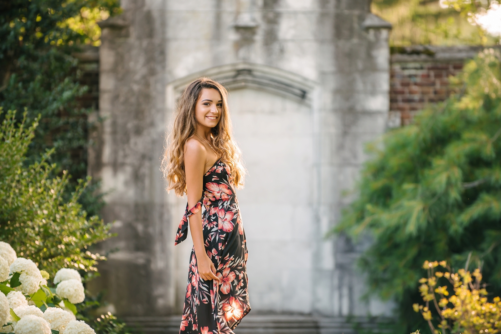 High school senior girl standing in front of stone wall at Mellon Park near Pittsburgh