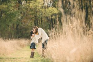Mom holding hands and kissing daughter in field at Sewickley Heights Borough Park near Pittsburgh