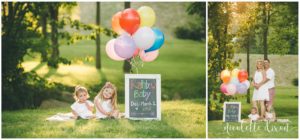 Girls sitting on blanket next to rainbow baby pregnancy announcement near Pittsburgh