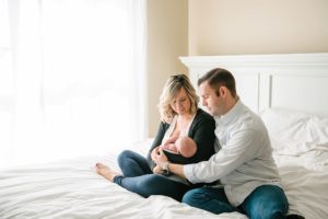 Mom and dad holding newborn baby girl on bed in home in Moon Township near Pittsburgh