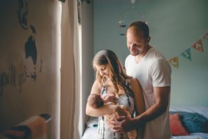 Mom and dad holding newborn baby girl by window in home in Robinson Township near PIttsburgh