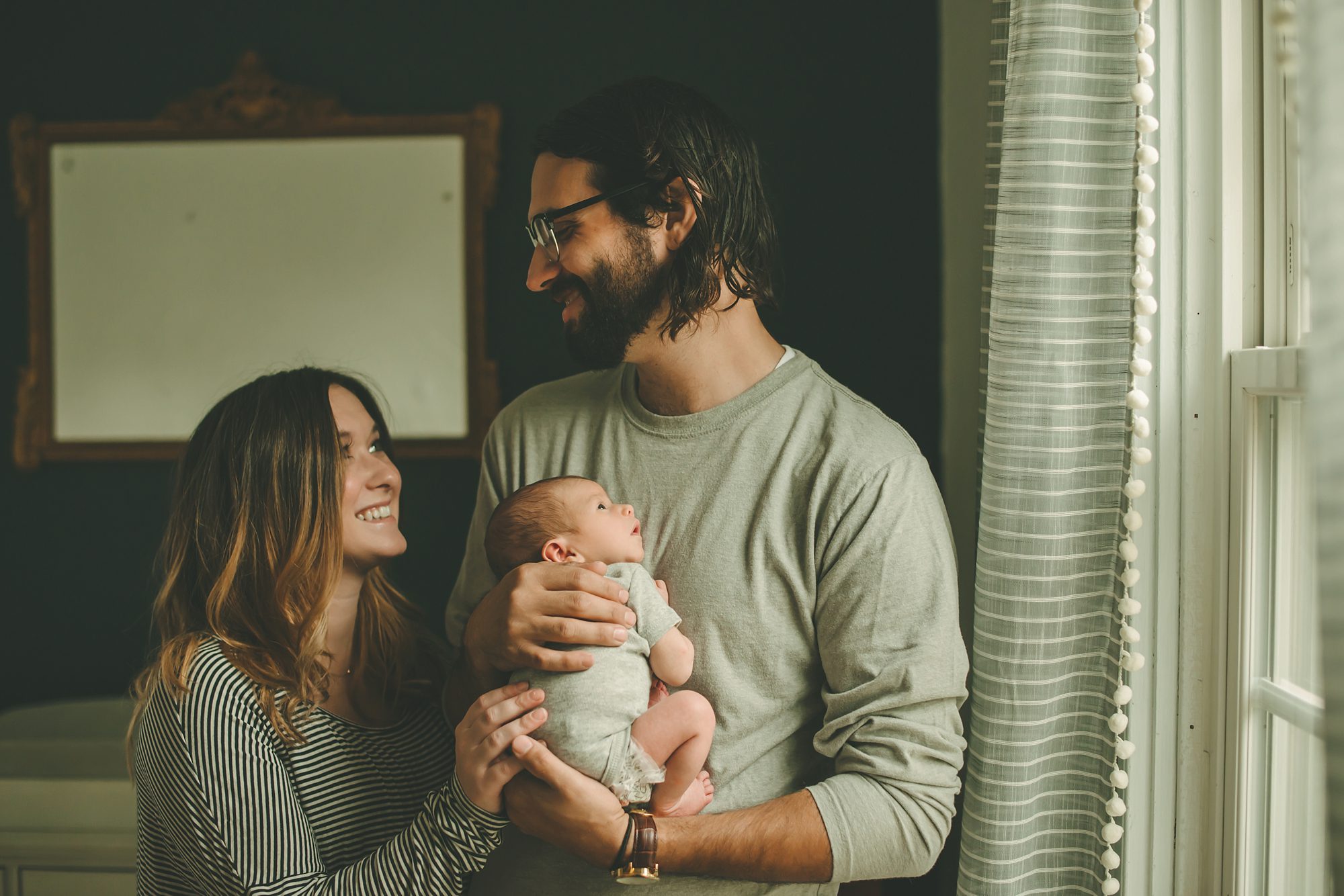 Mom and dad holding newborn baby boy by window in home in Coraopolis near Pittsburgh