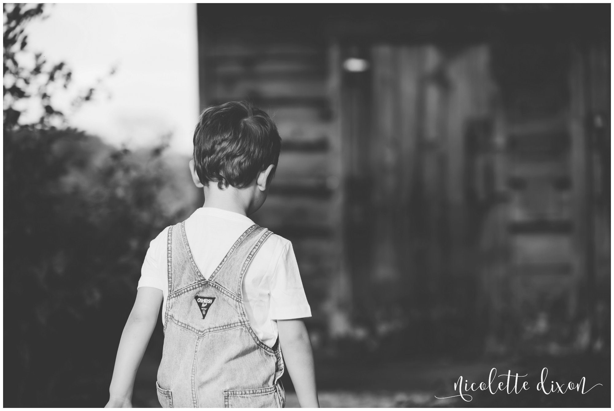 A black and white of a young boy in overalls playing near a barn at Round Hill Park near Pittsburgh