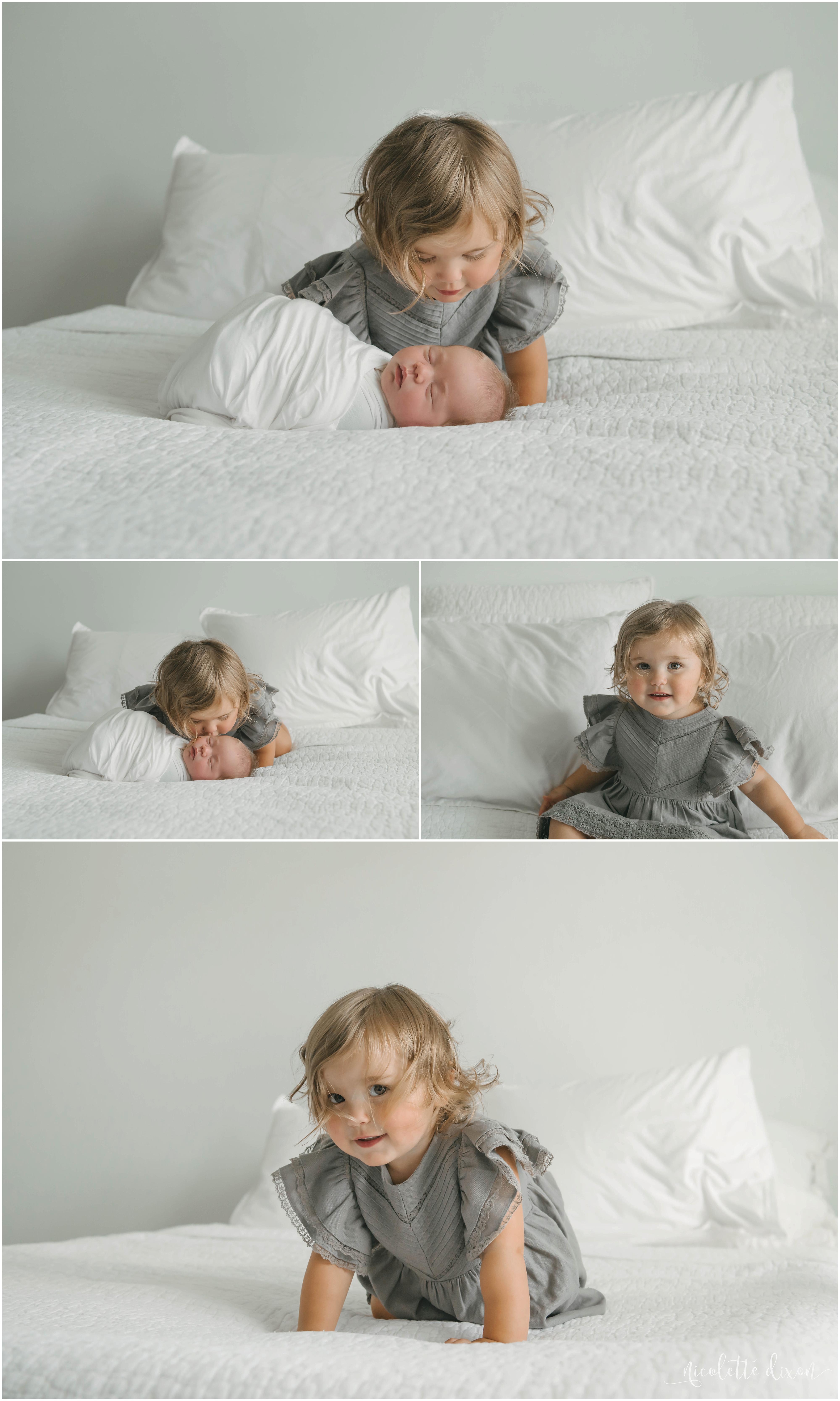 Little girl kissing newborn baby sister on bed in studio in Moon Township near Pittsburgh