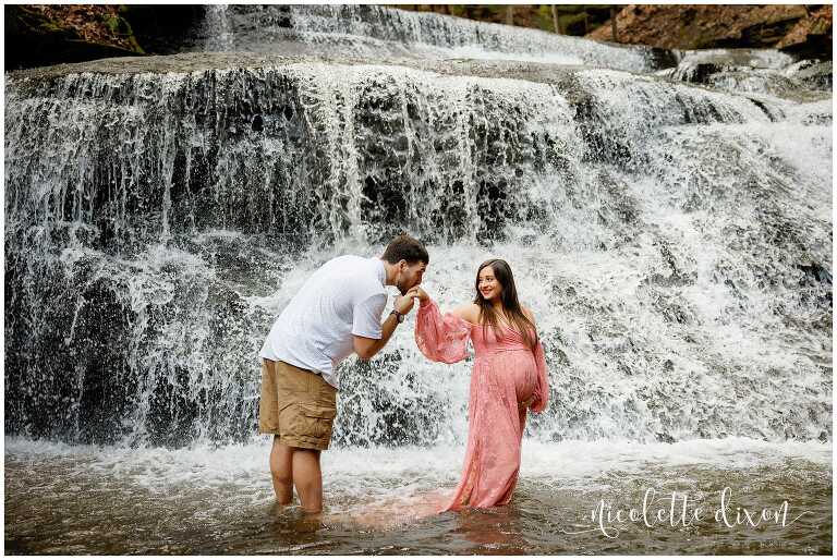 Man kissing pregnant womans hand in waterfall