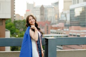 College graduate holding gown over shoulder in front of Pittsburgh skyline at Duquesne University