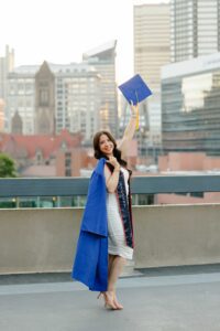 College graduate holding up cap in front of Pittsburgh skyline at Duquesne University