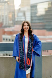 College graduate standing in front of Pittsburgh skyline at Duquesne University