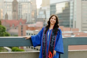 College graduate standing in front of Pittsburgh skyline at Duquesne University