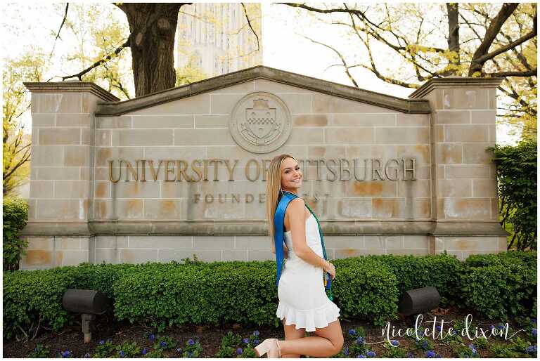 College grad standing in front of the University of Pittsburgh sign