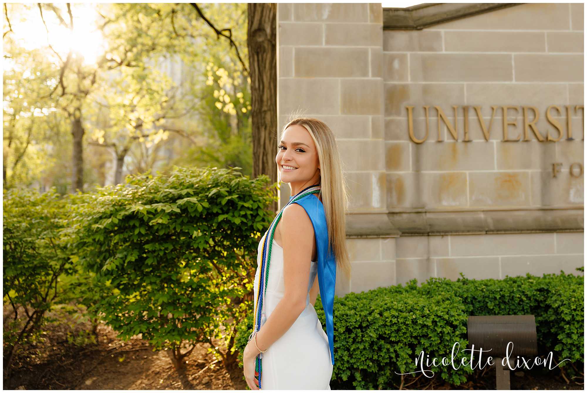 College grad standing in front of the University of Pittsburgh sign