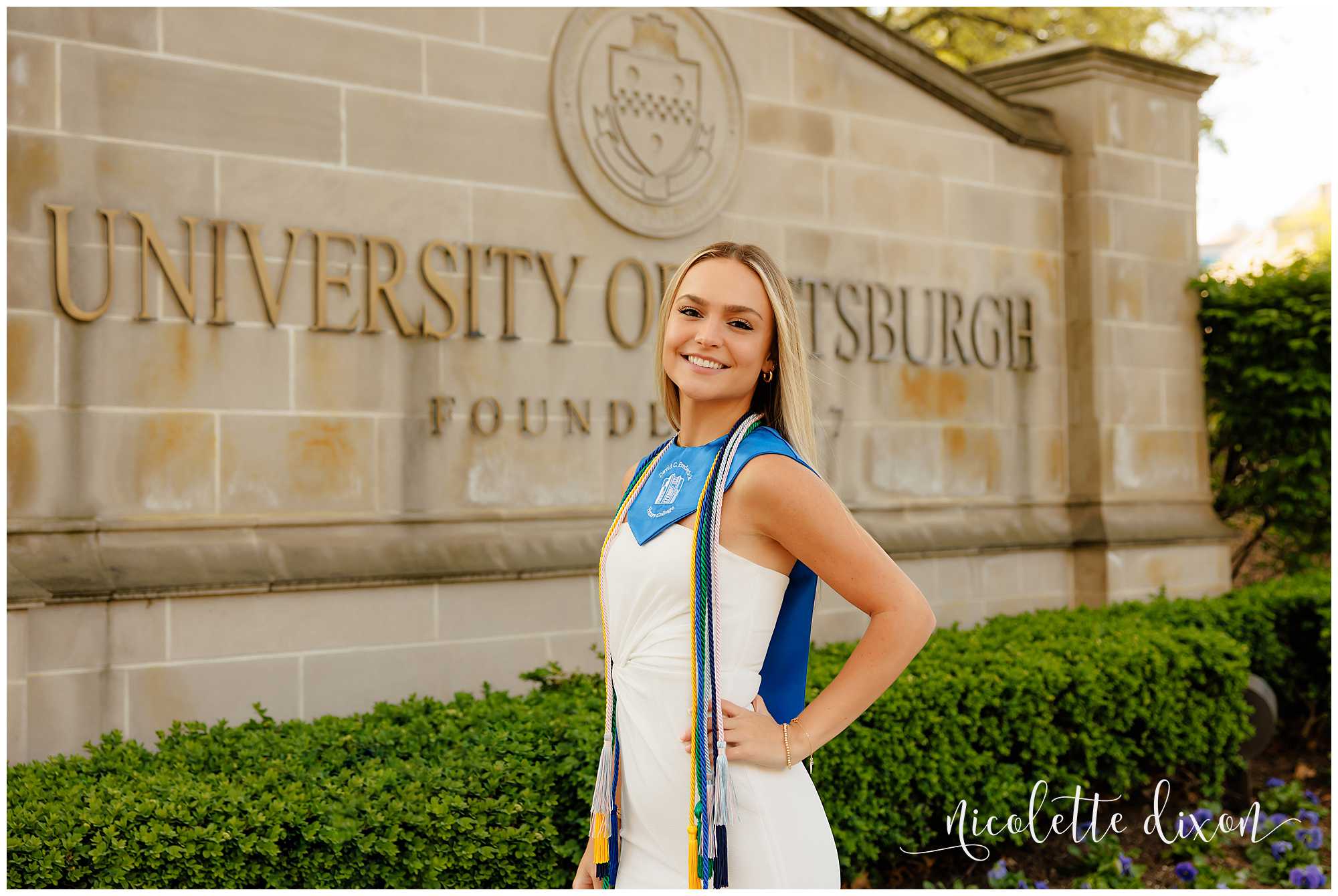 College grad standing in front of the University of Pittsburgh sign