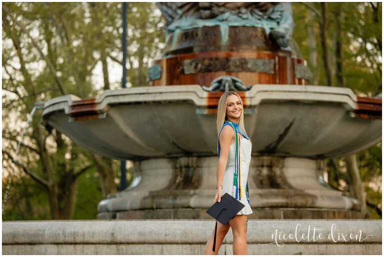 College grad standing in front of the Mary Schenley Memorial Fountain at the University of Pittsburgh
