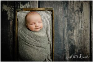 Newborn baby boy wrapped in green blanket in wooden box in studio in North Fayette Township near Pittsburgh.