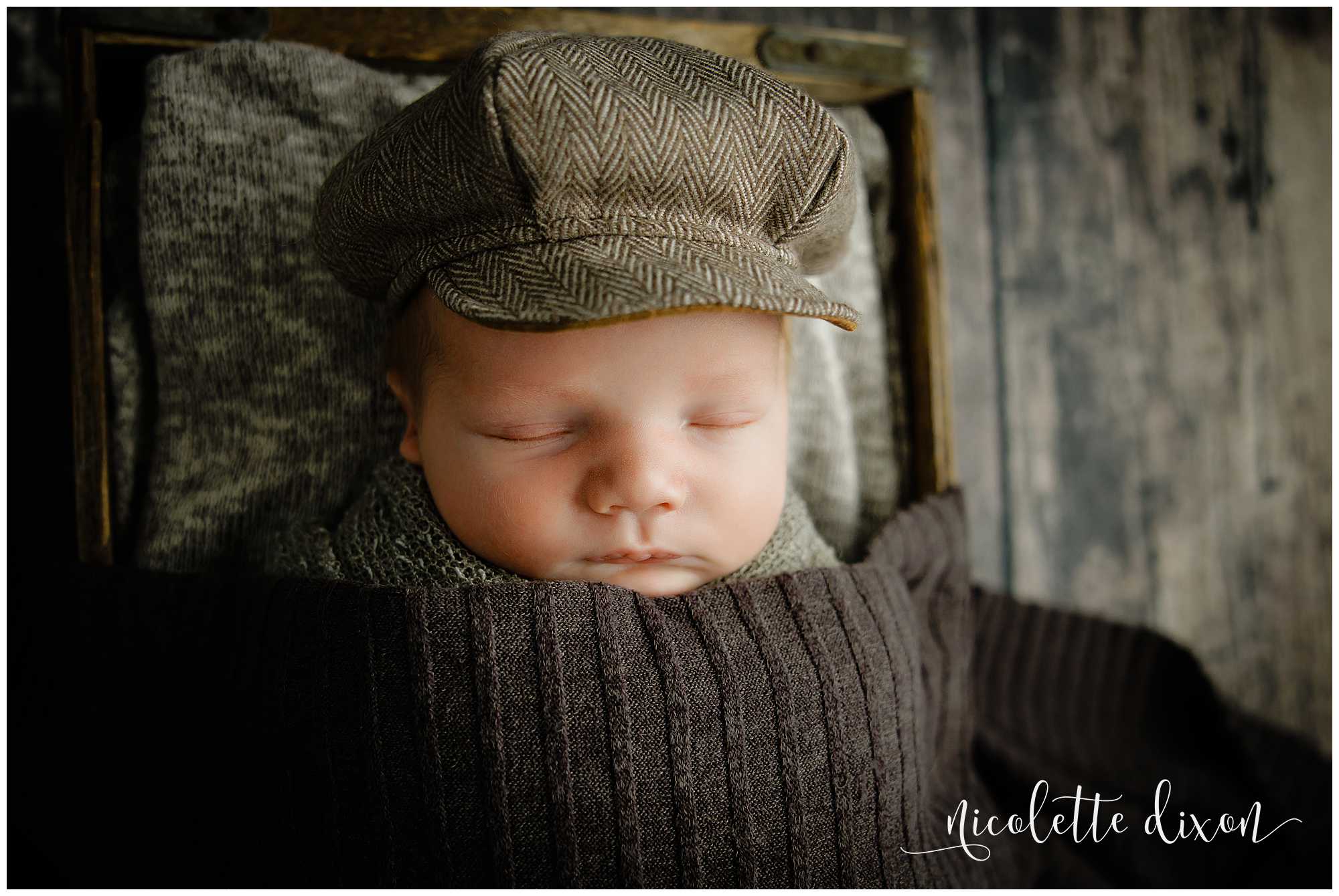 Newborn baby boy wearing hat and covered in brown blanket in studio in North Fayette Township near Pittsburgh.